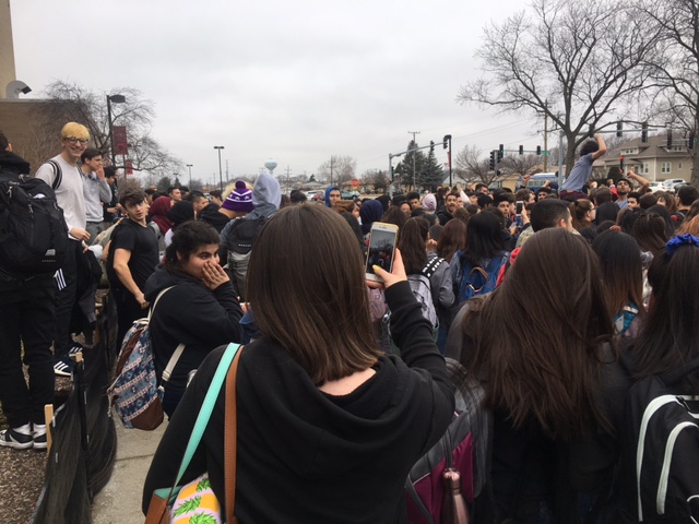 Students gather around the front of the school, carrying a student, and chanting, No more guns! 