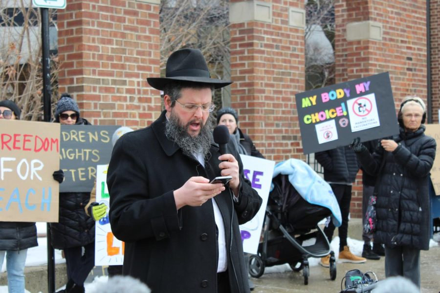 The rabbi speaks in front of cameras and the crowd, relating current events to Jewish history, both recent and that documented in the Torah.