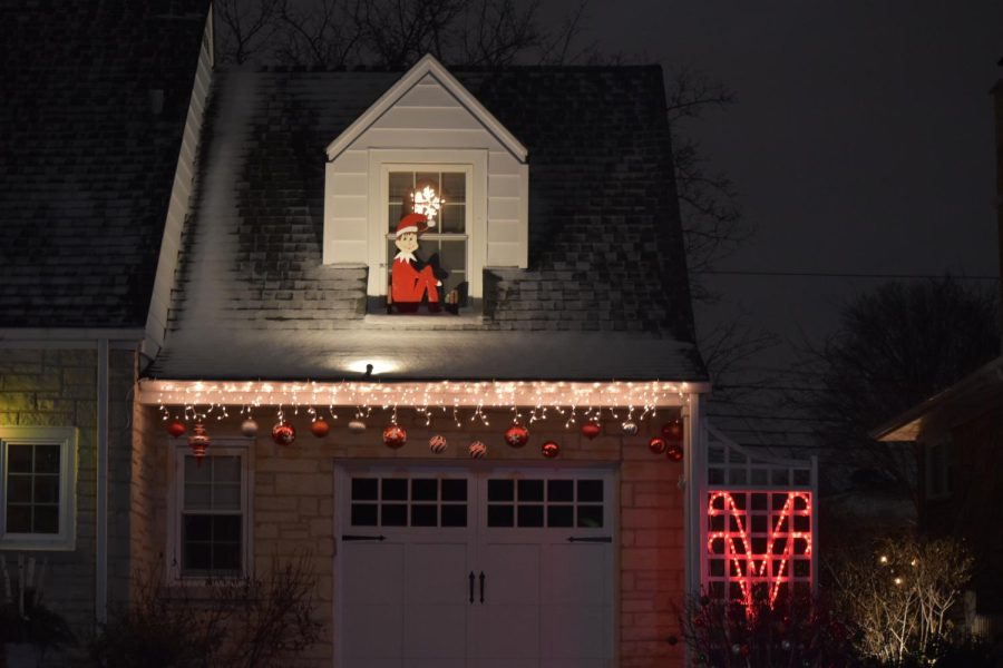 A cutout of the Elf on the Shelf hangs out of the window sill above the garage. 