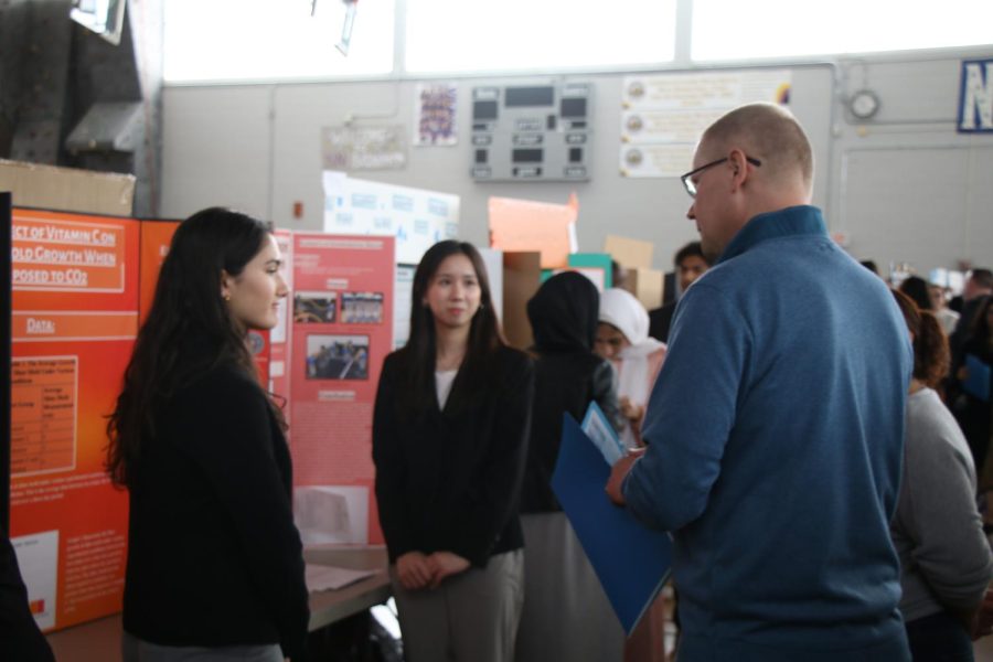 Senior Sophia Lannoye and junior Charlize Chung at their poster boards, as guests walk by. 