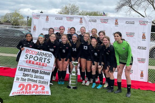 Girls varsity soccer pose with their 2023 Body Armor Tournament champion trophy and poster. 
