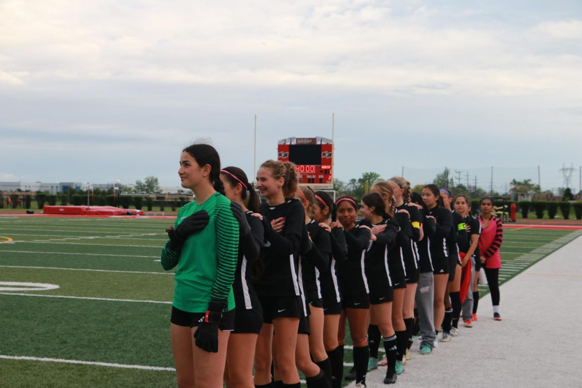 Niles West girls varsity stands together and place their hand over their chest for the pledge of alligence.