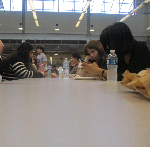 Students sit around a lunch table conversing, eating and scrolling on their phones.