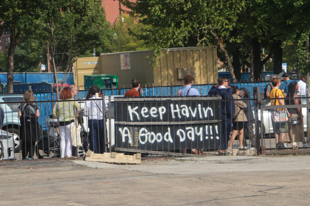 A spray painted piece of wood remarking, "Keep Havin A Good Day!!!" It stands in front of the line to get inside the DNC.