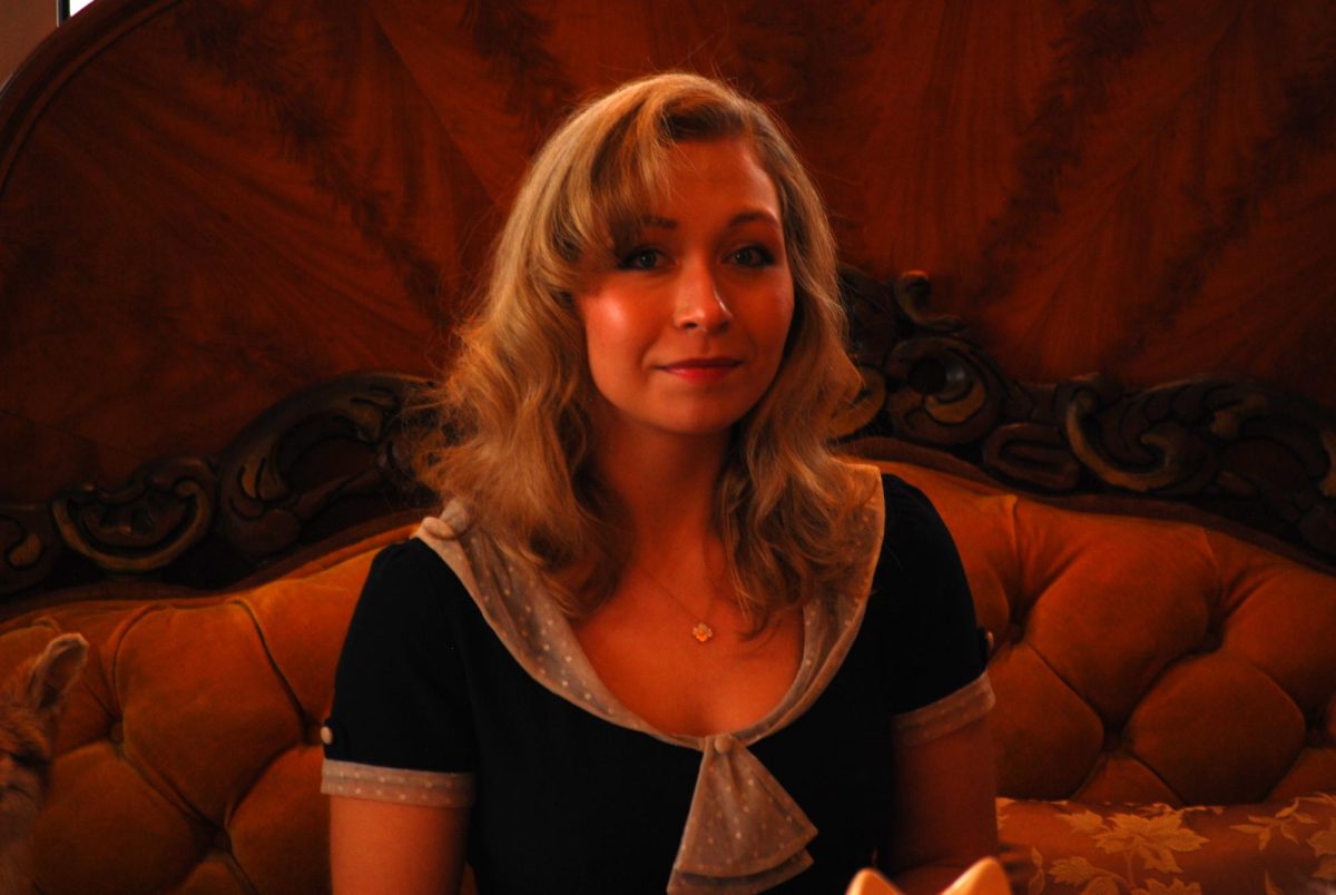 A portrait of store owner Kayla Carpenter. She sits on an antique velvet couch.