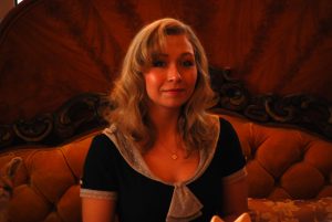 A portrait of store owner Kayla Carpenter. She sits on an antique velvet couch.