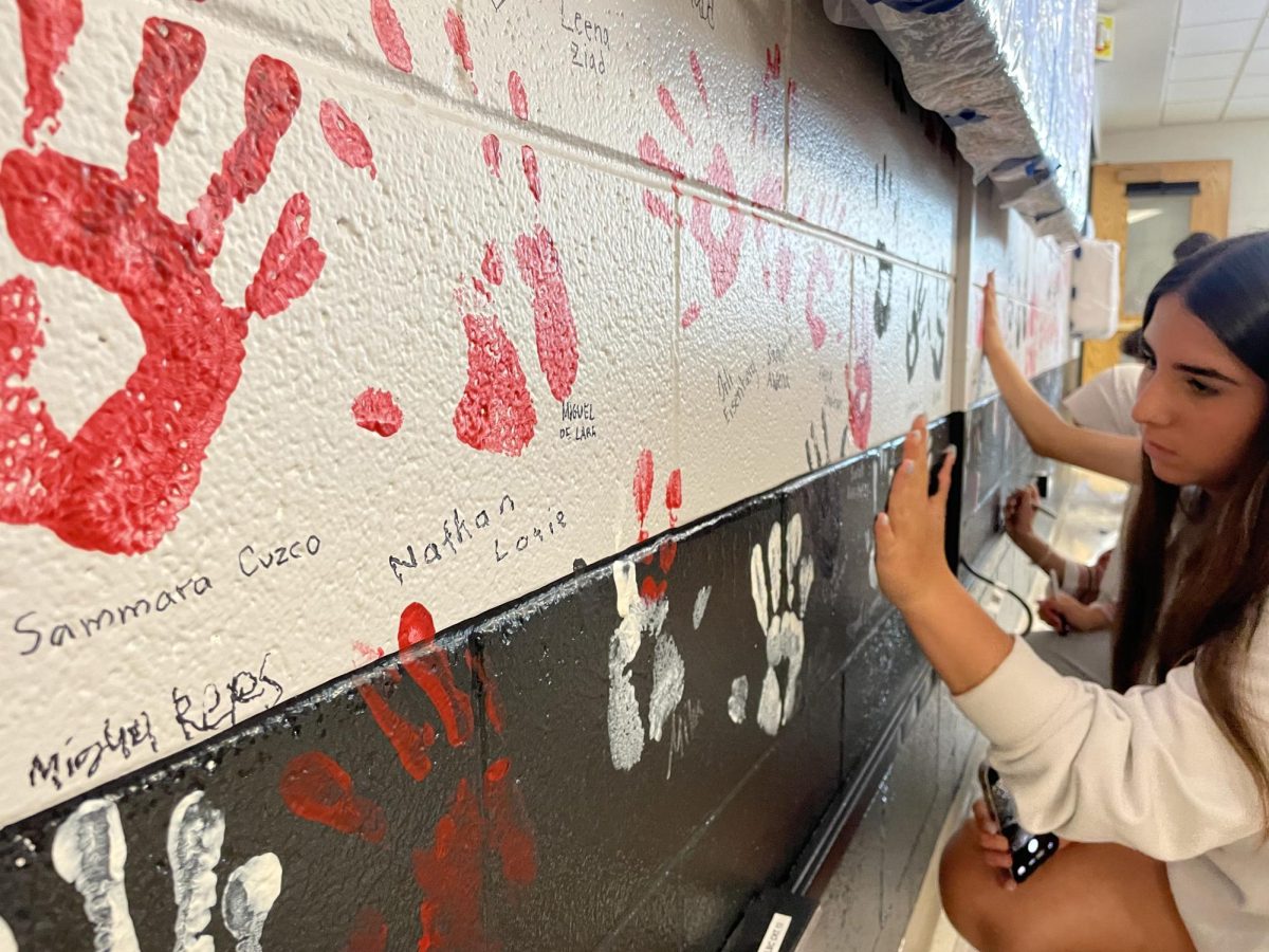 A senior lifts up their hand from the wall, leaving behind a black paint handprint.