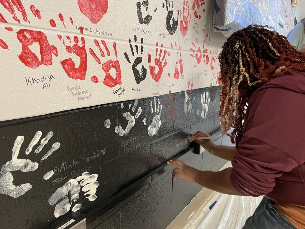 Neeptah Frost, senior, writes her name on the senior alley wall after imprinting her hand with red paint into the wall. 